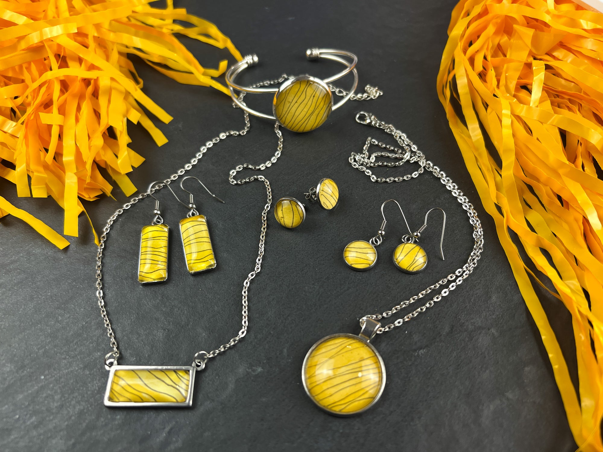 Pieces from the Tiger Stripe collection of watercolor jewelry by JL Scheppers Art. Each necklace, bracelet or pair of earrings shows the same wavy black ink over golden yellow watercolor paint. 