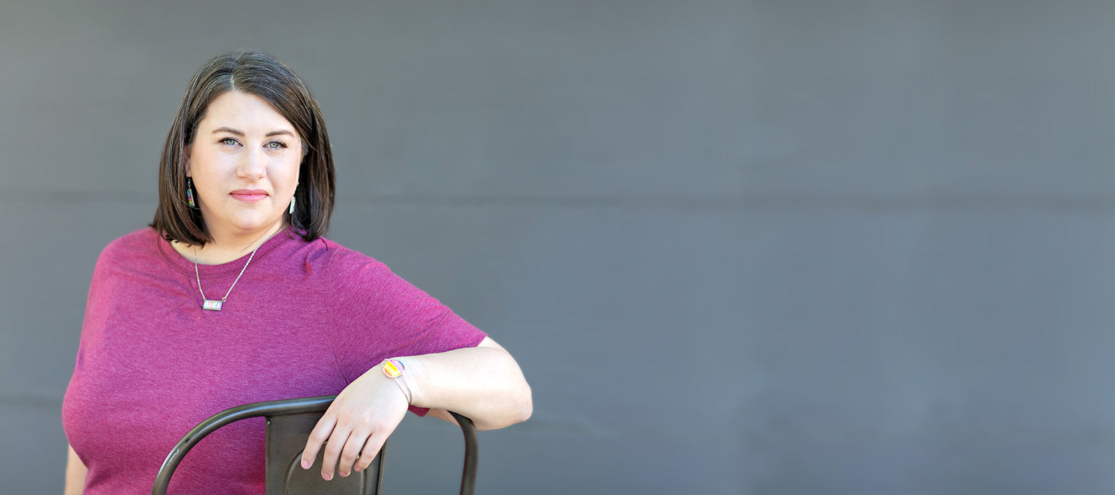 Portrait of Jamie Scheppers sitting in a chair in front of a grey background. 