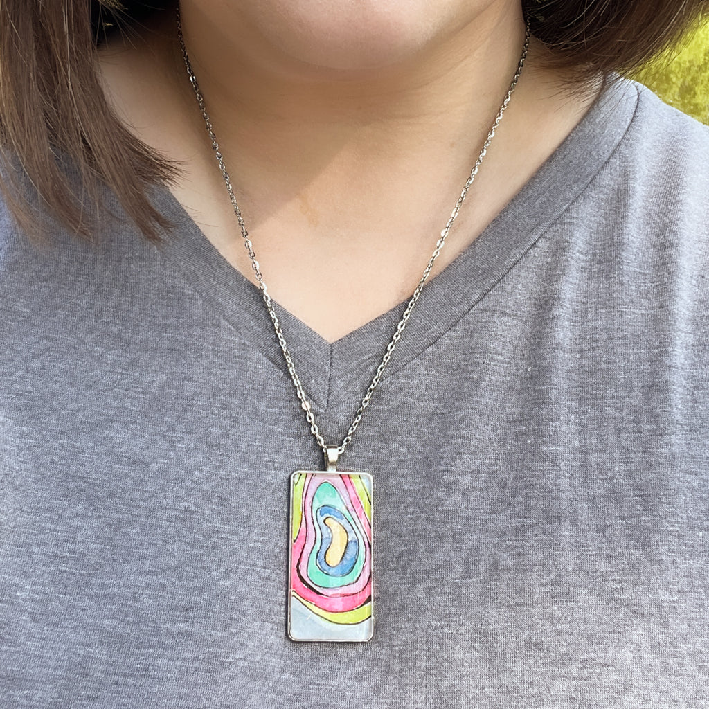 Hand-painted watercolor pendant with concentric rings of bright colors on a pale blue background. 