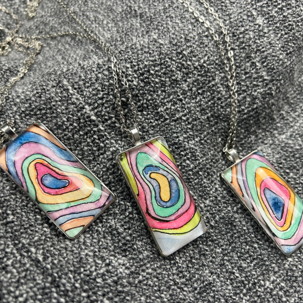 Selection of Topo and Elevation Pendants on a grey blanket. 