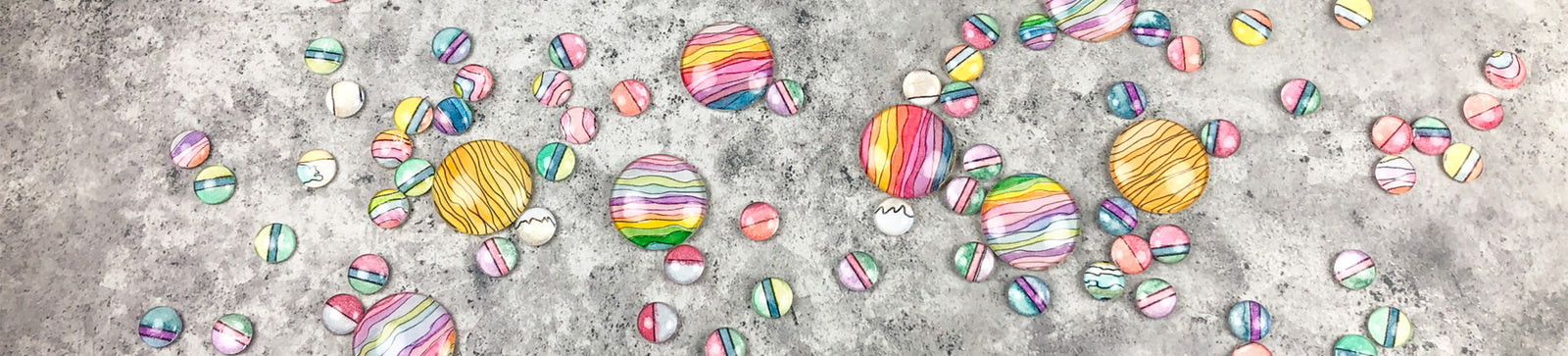 Image of watercolor paintings behind glass cabochons scattered on grey table.