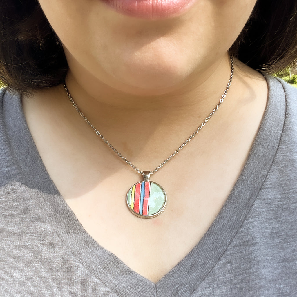 Close-up of the Huntleigh Round pendant which features red and green prominently along with blue and yellow in a series of vertical stripes. 