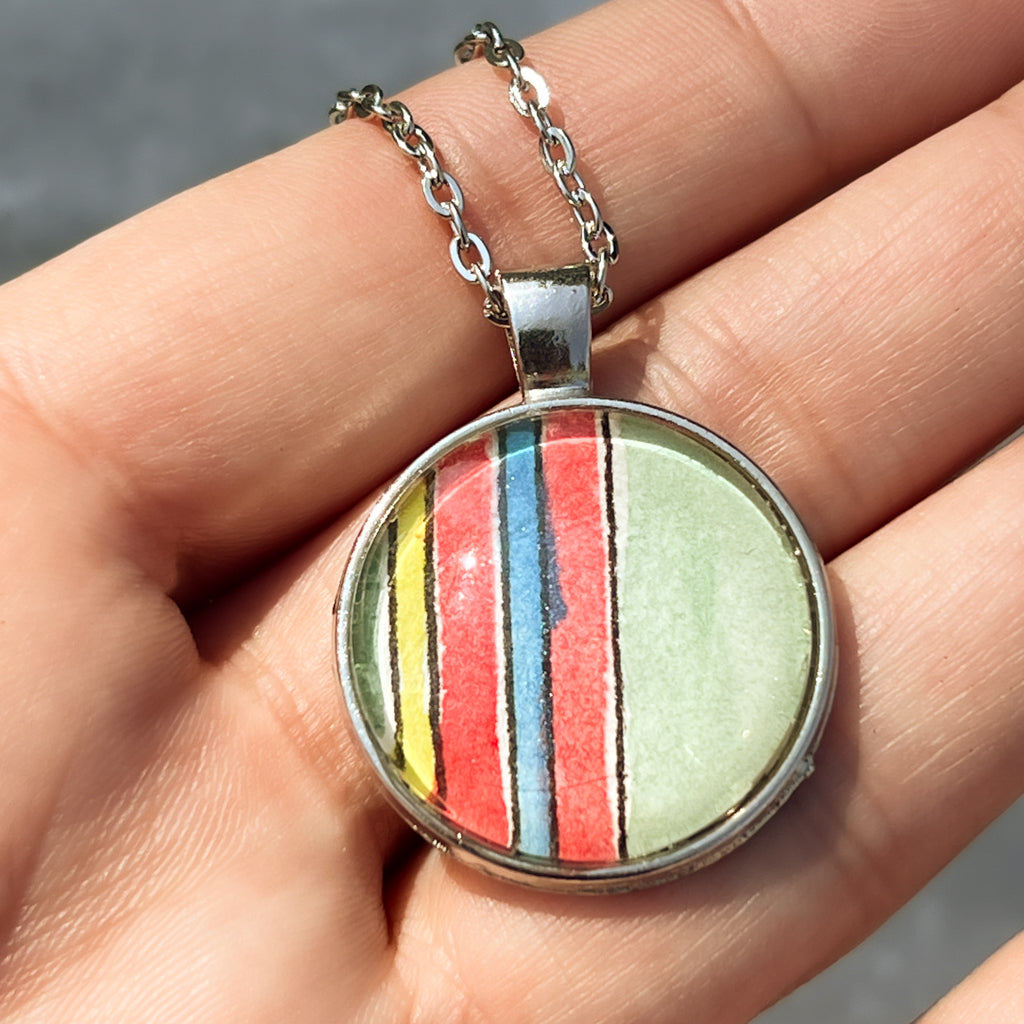 Huntleigh round watercolor pendant shown up close in the hand. 