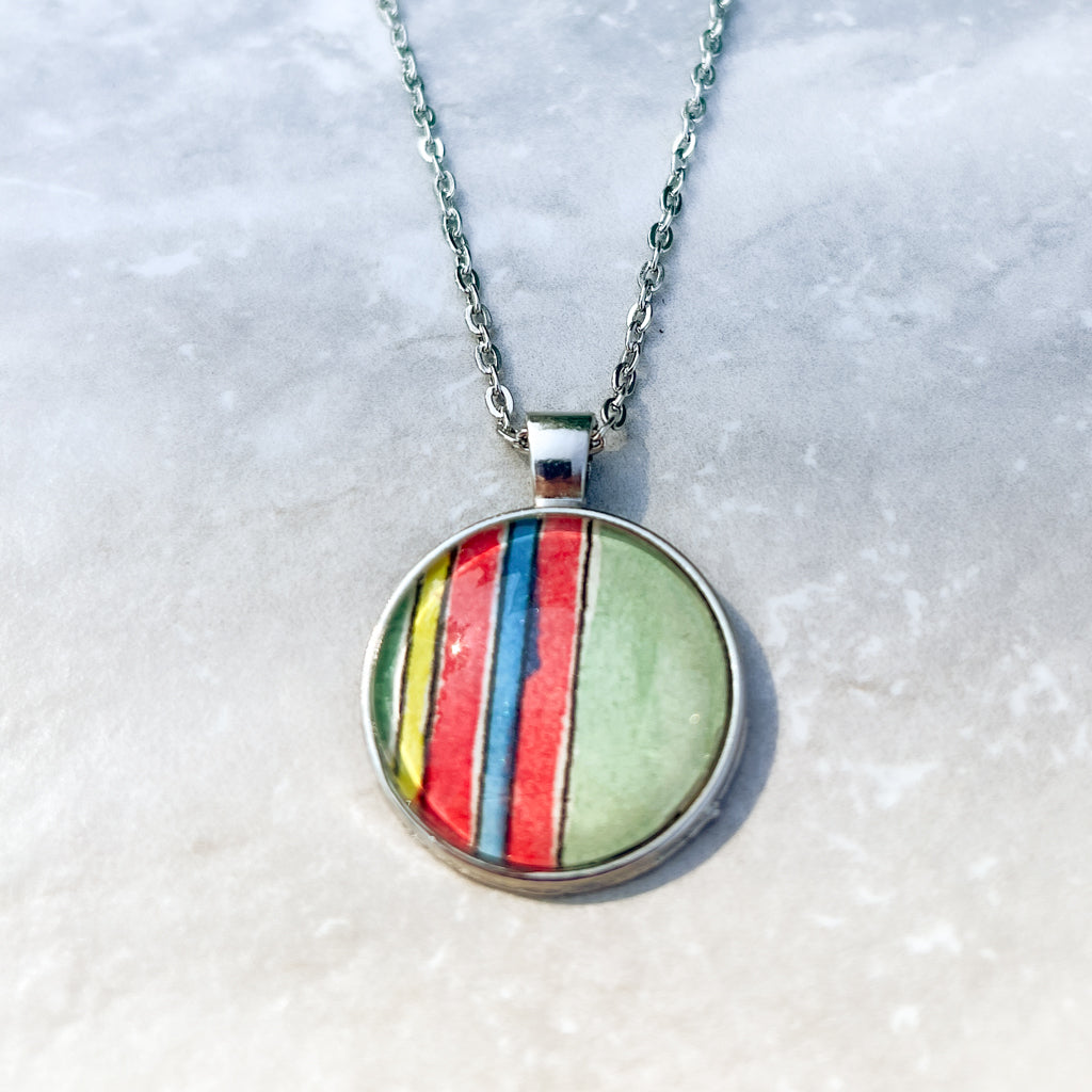 Close-up of the Huntleigh Round pendant which features red and green prominently along with blue and yellow in a series of vertical stripes. 