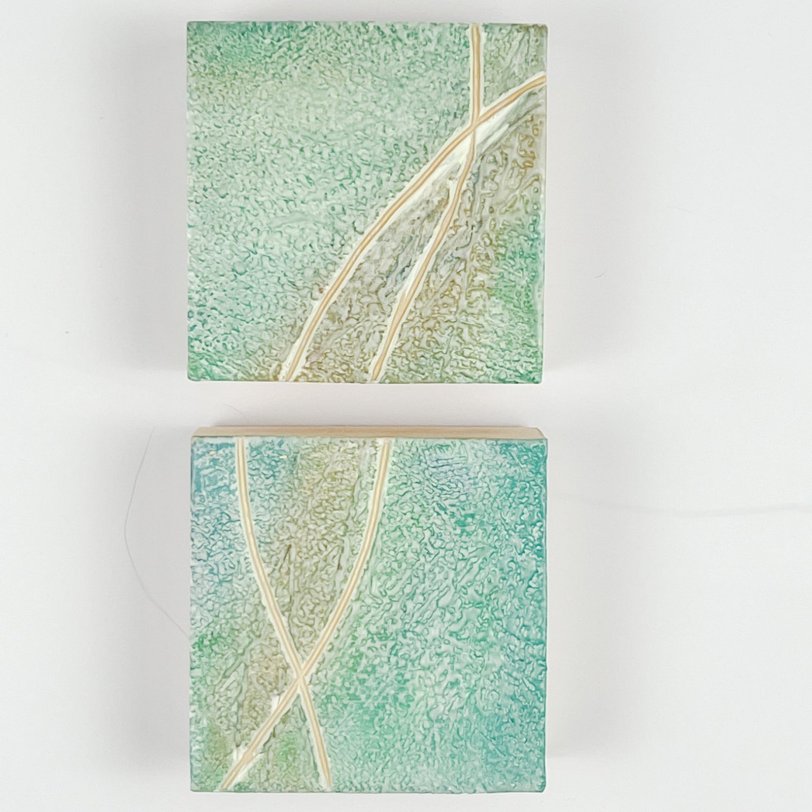 Two light seafoam-colored textured encaustic paintings. Each is 4" by 4."