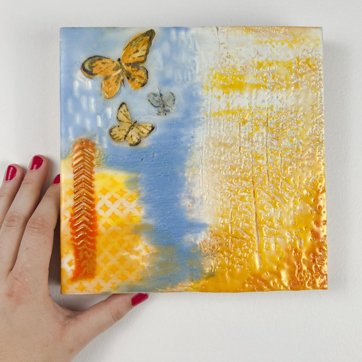 Peace for Ukraine encaustic painting in light blue, yellow/gold, and featuring fabric butterflies. 