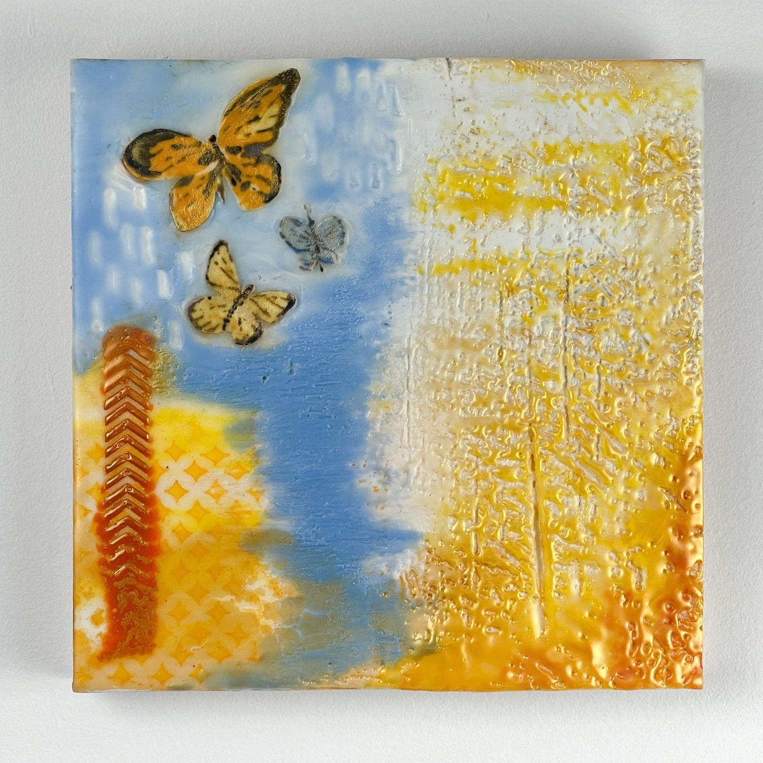 Peace for Ukraine encaustic painting in light blue, yellow/gold, and featuring fabric butterflies. 