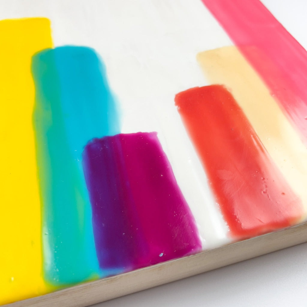 10" by 10" encaustic painting featuring vertical striped of paint on a white background layered to resemlble the buildings in a skyline. 