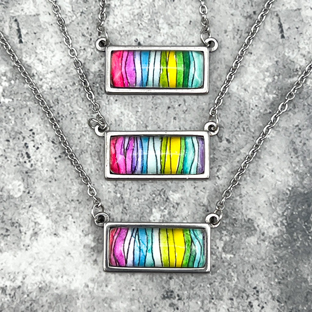 Three spectrum pendants stacked vertically. Each pendant  has colors ranging form pink to blue, green, and yellow.