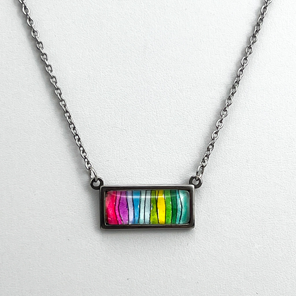 Closeup of  asingle multi-color horizontal spectrum necklace on a white background.  The pendant has pinks, blues, yellows and greens. 