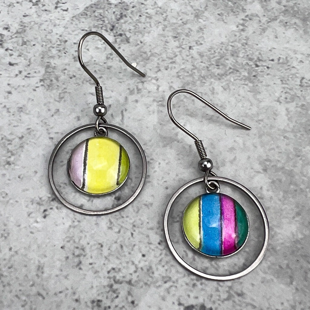Half-inch circles of watercolor art protected behind glass cabochons in stainless steel settings. Surrounded by circular frames and displayed on a grey background.