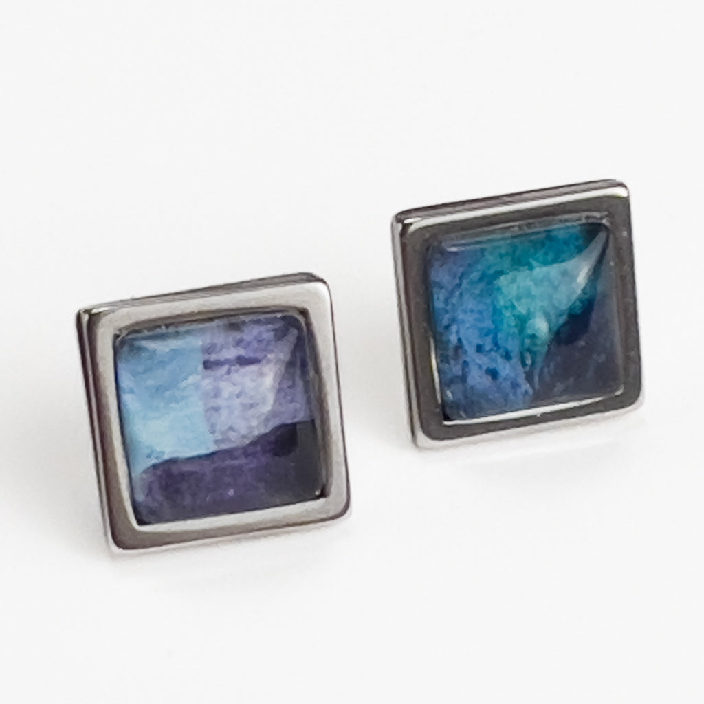 Square stud earrings with Blue Superfly art. White background.