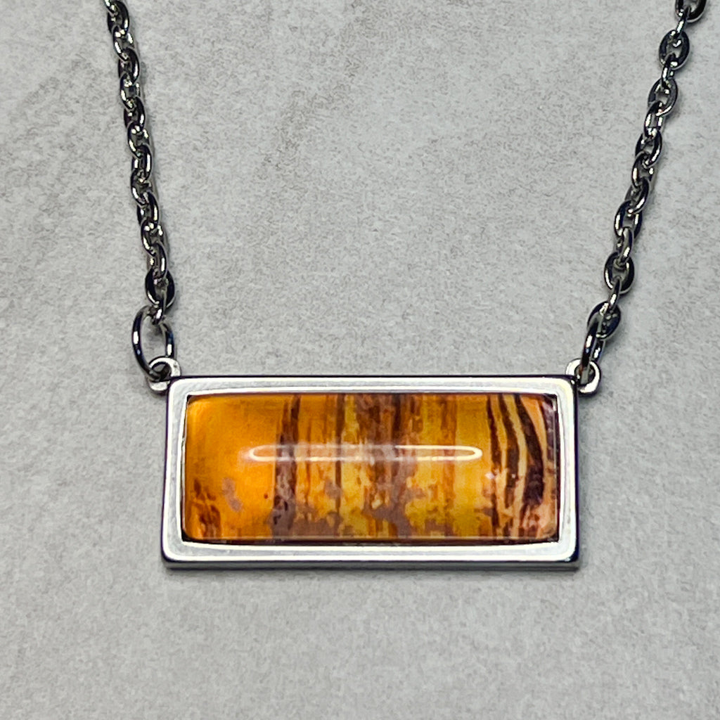 Horizontal rectangular necklace featuring orange watercolor art behind a glass cabochon. 