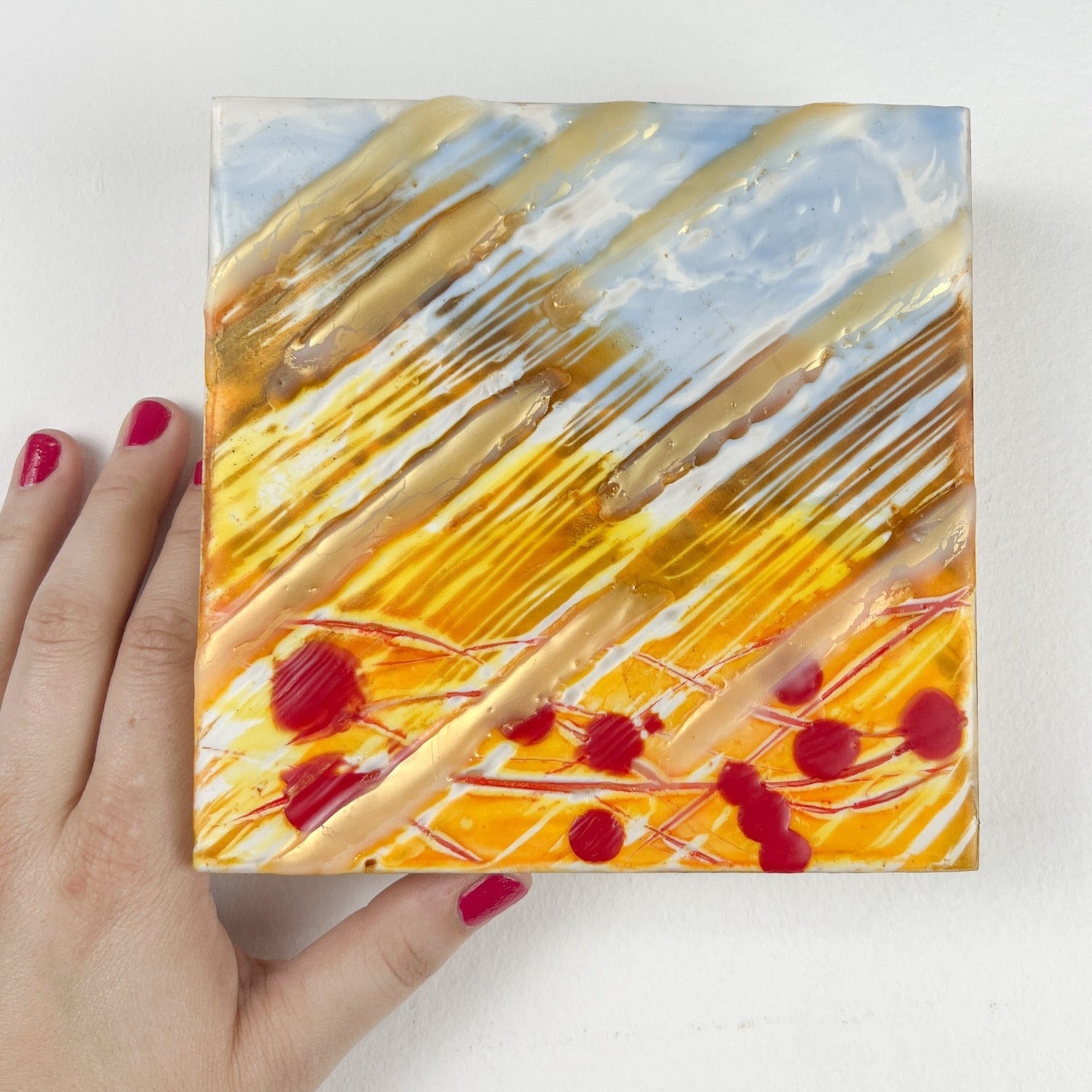 Close up of 6" square encaustic painting in yellow/gold and blue, with red "blood" drops. 