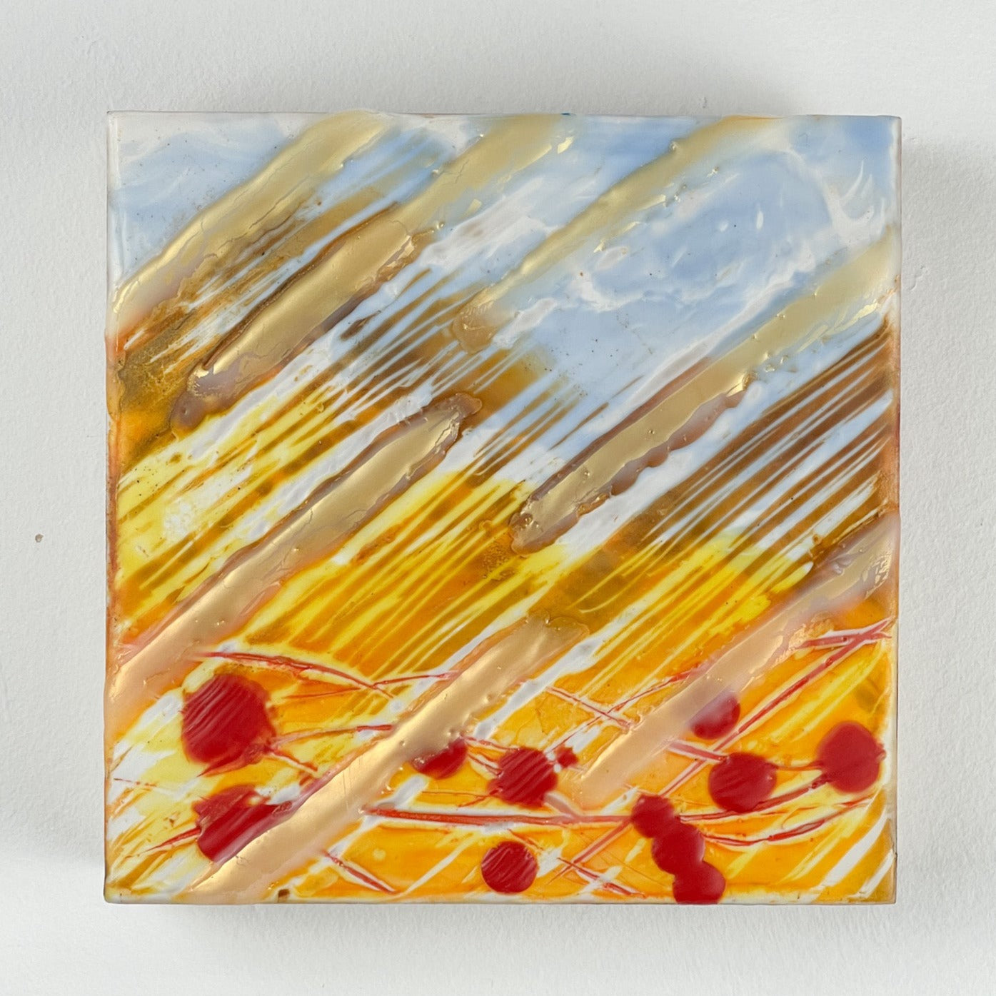 Close up of 6" square encaustic painting in yellow/gold and blue, with red "blood" drops. 