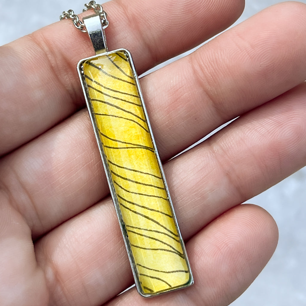 Narrow rectangular pendant in with black ink and golden yellow watercolor paint. 