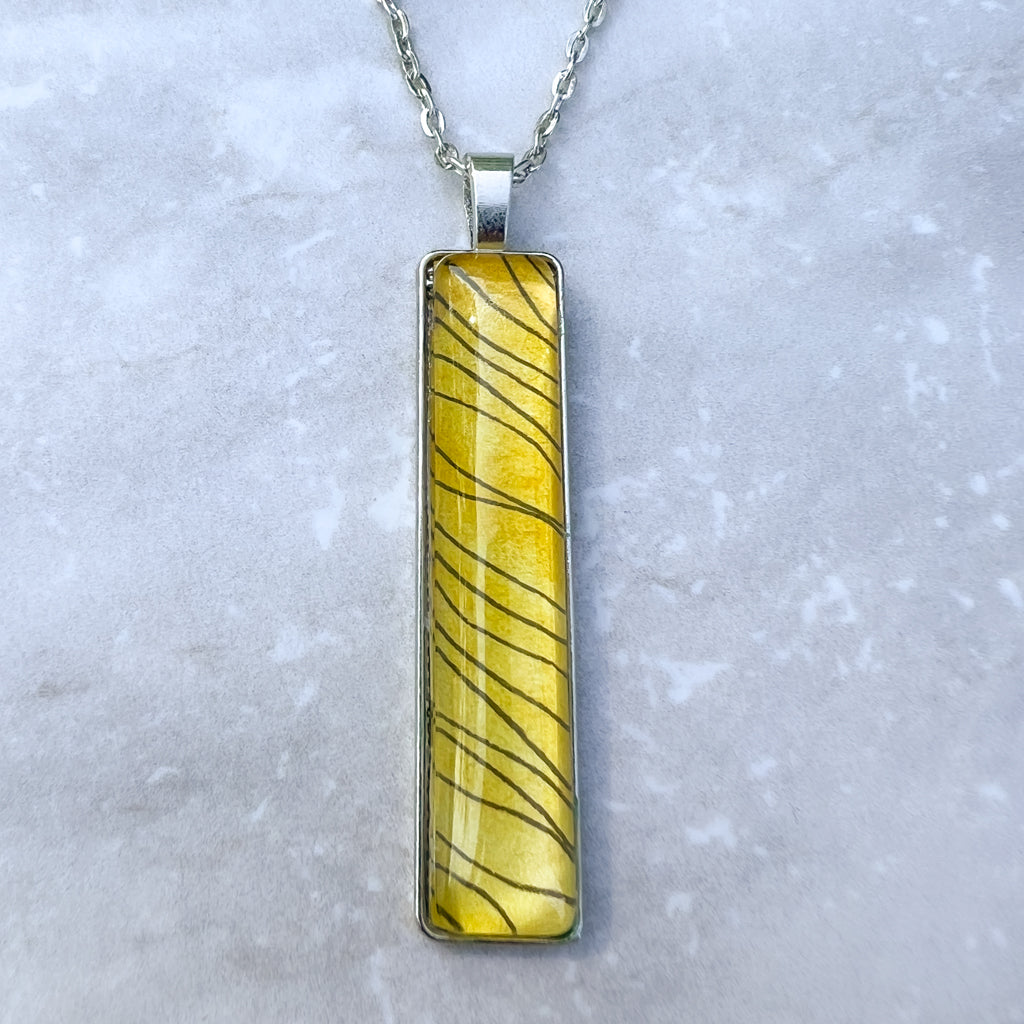 Narrow rectangular pendant in with black ink and golden yellow watercolor paint. 