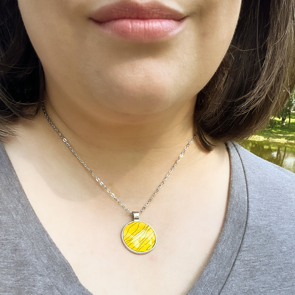 Close up of round black and gold Tiger Stripe watercolor pendant. 
