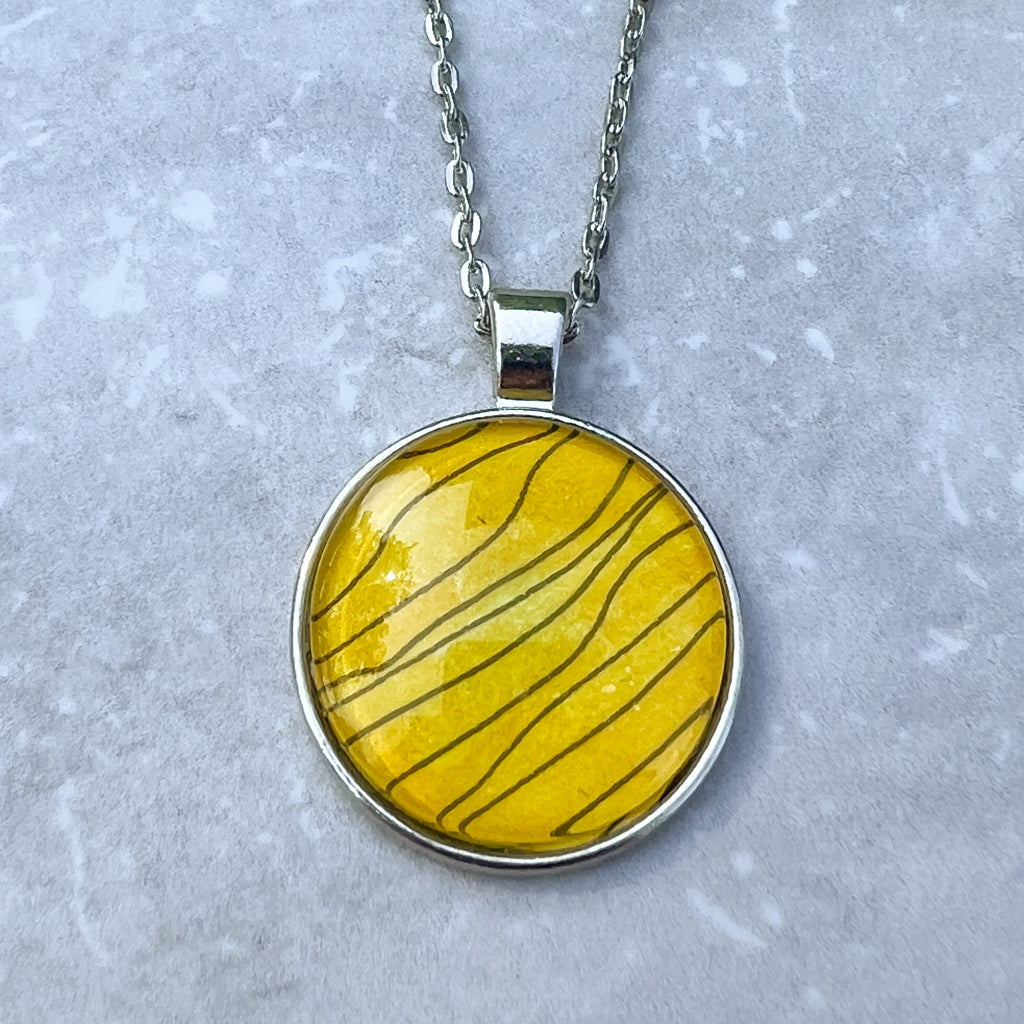 Close up of round black and gold Tiger Stripe watercolor pendant. 