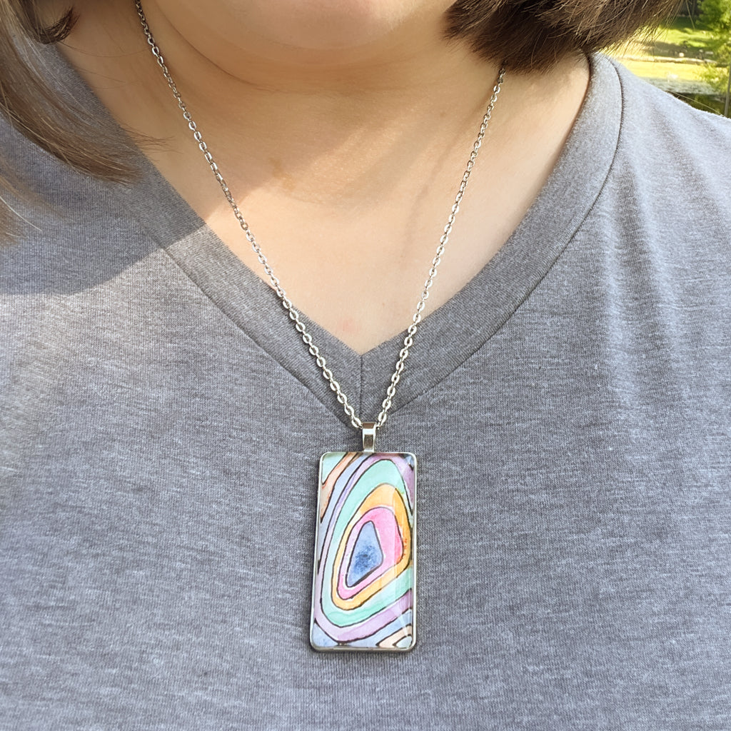 Closeup of Topo pendant which features multi-solor rings of watercolor paint that resemble a topographical map. 