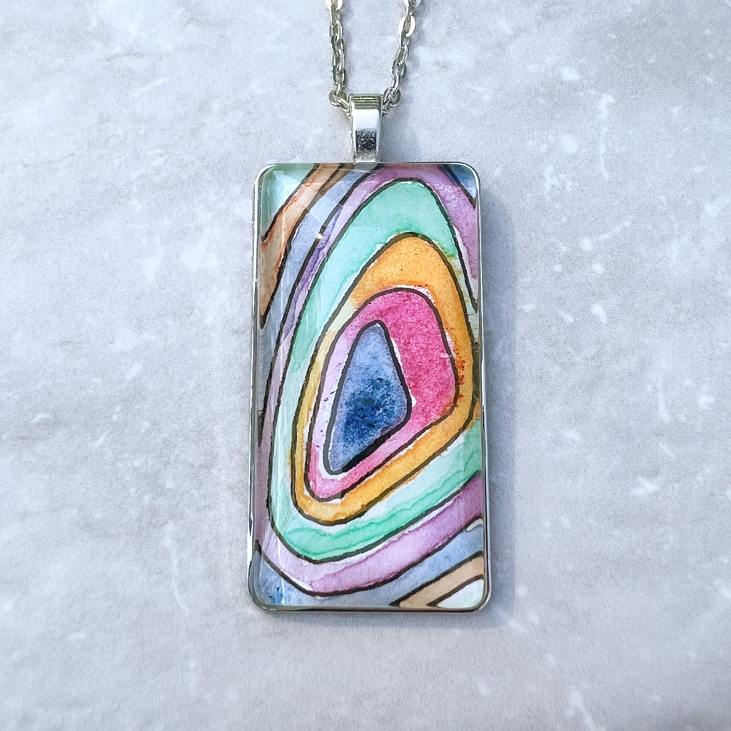 Closeup of Topo pendant which features multi-solor rings of watercolor paint that resemble a topographical map. 