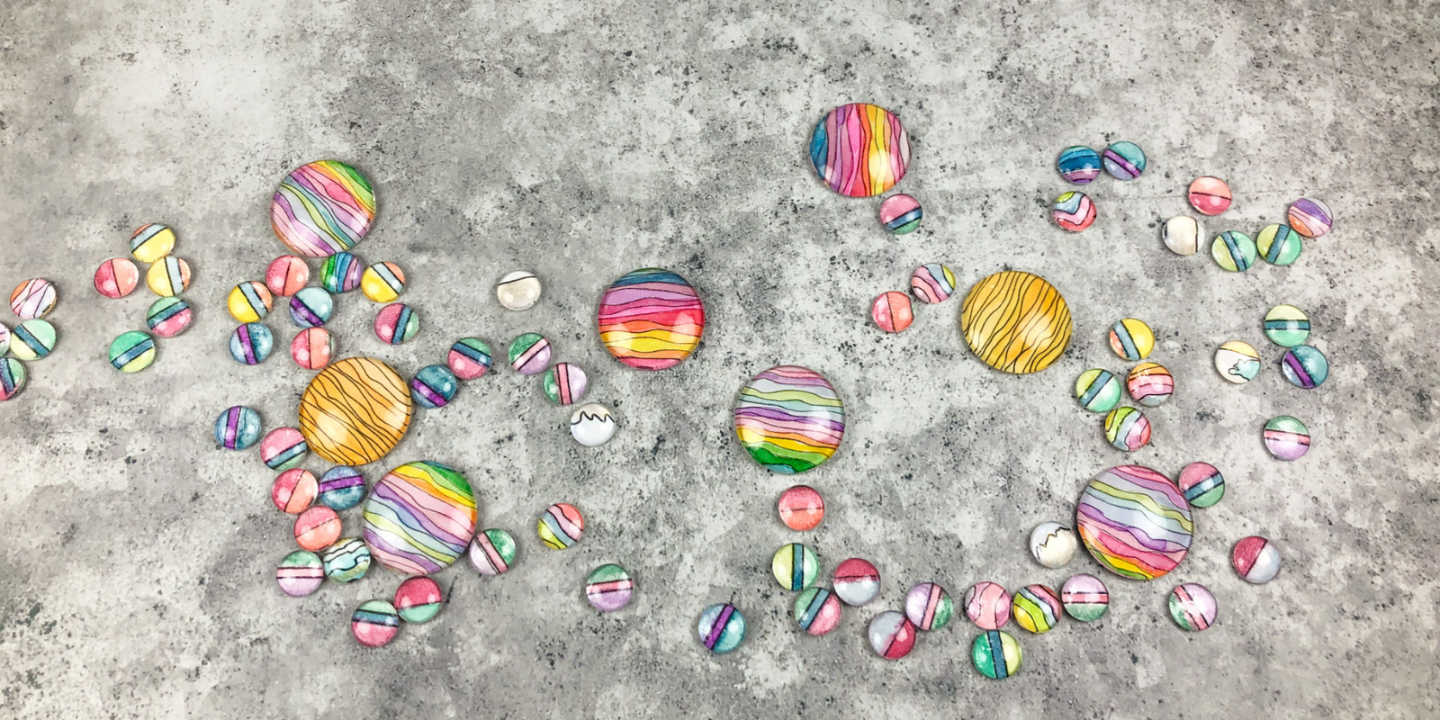 Hand painted watercolor cabochons scattered on a grey background. 